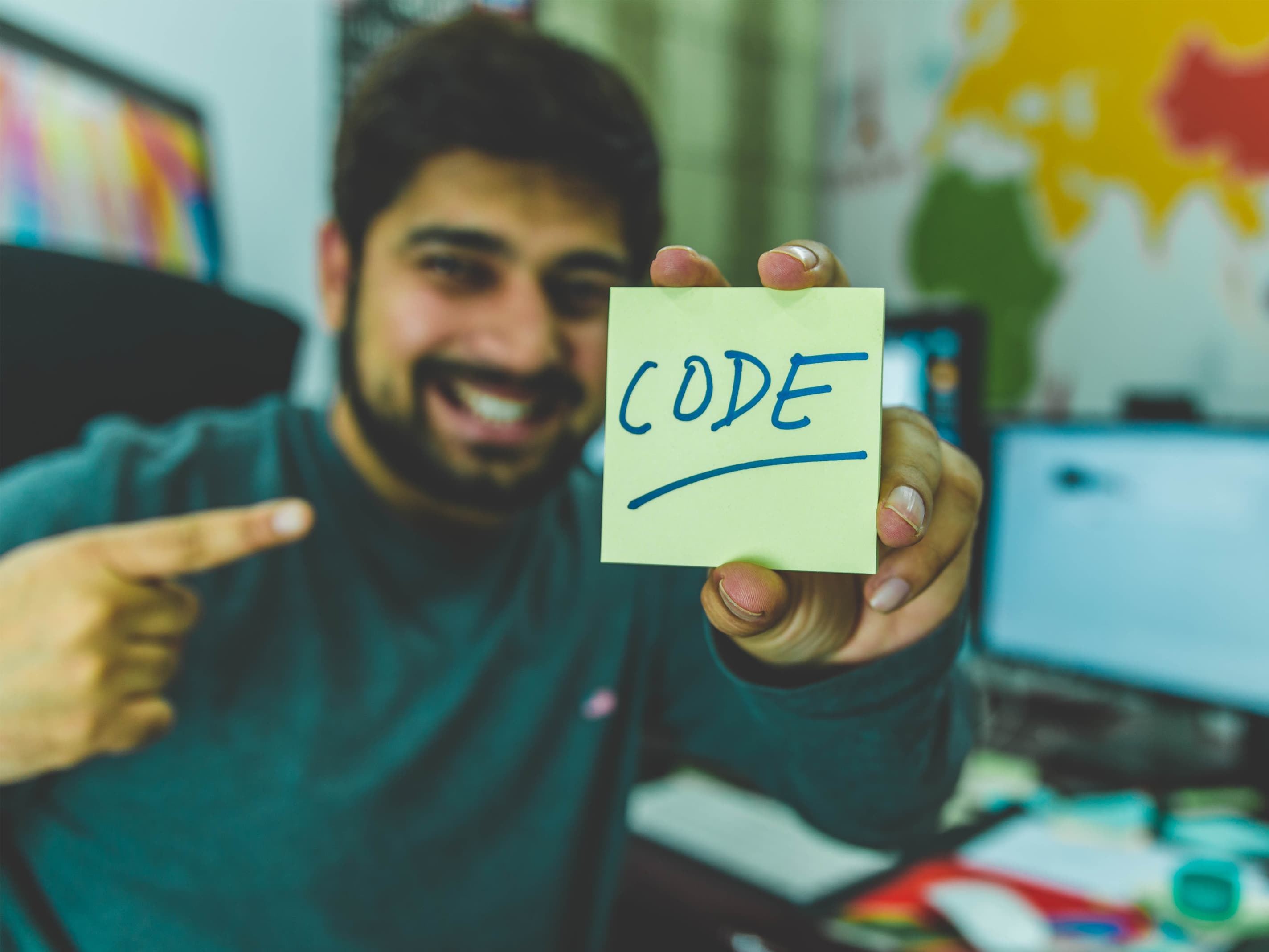 Photo of a man holding up a post it note with the word code in the middle.
